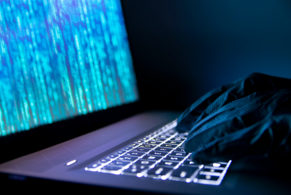 Imagen de manos de un ciberdelincuente con guantes negros digitando un teclado de un portátil encendido. Imagen de manos de un ciberdelincuente con guantes negros digitando un teclado de un portátil encendido.